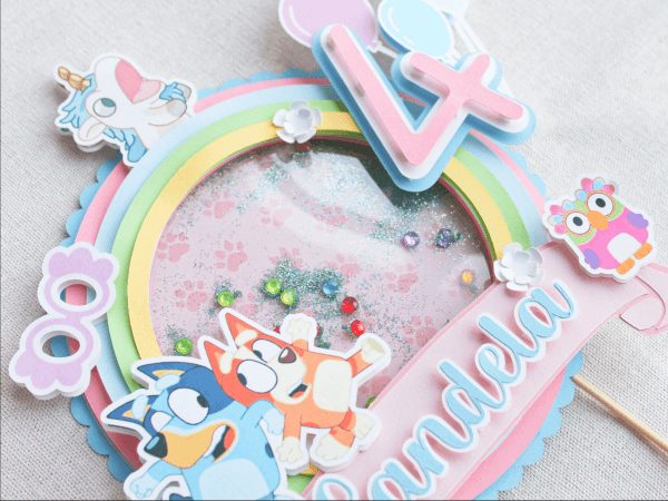 Topper para tarta personalizado, en 3D y temática Bluey. Colores Rosa, Azul y Blanco. Con motivos de los personajes, Nombre y años.